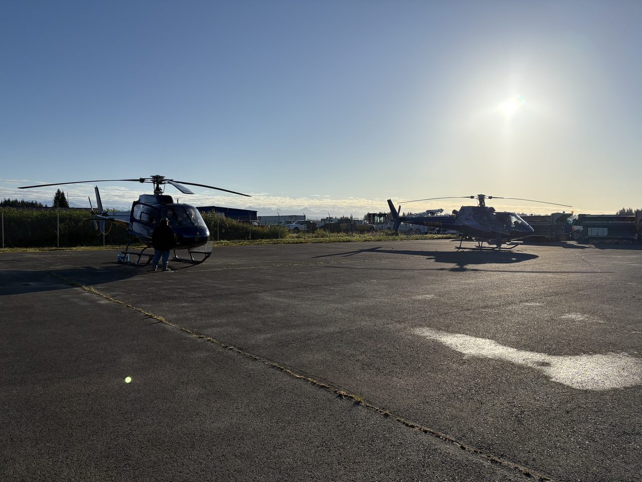 Anglers with a wheelbarrow of salmon beside a helicopter on a rainy ramp.